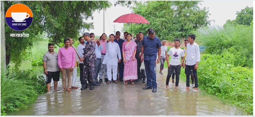 Anupriya Patel visiting flood-hit areas in Uttar Pradesh with officials and locals, standing in water under a red umbrella